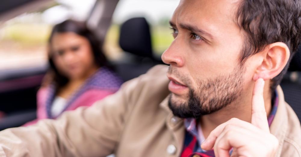 A man sits in the driver's seat of a car while listening carefully for something. A woman sits next to him.