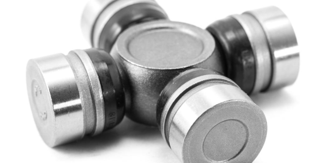 A silver universal joint bearing with four cylindrical ends rests on a plain white surface at an angle.