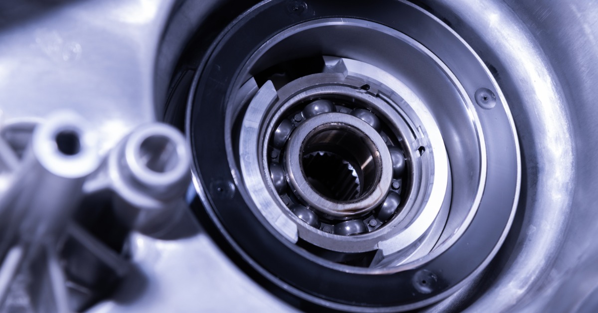 A close-up of a circular metal ball bearing inside of a silver mechanical housing. Blurred rounded parts are to the left.