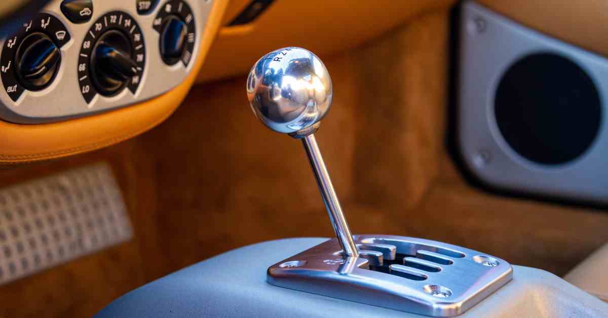 A tan interior of a vintage car with a chrome stick shifter in the center and air conditioning controls to the left.