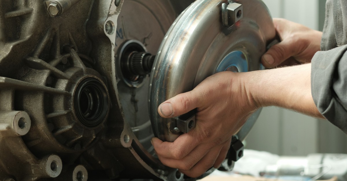 Close-up of a car's automatic transmission. A mechanic's hands install a torque converter onto the transmission.