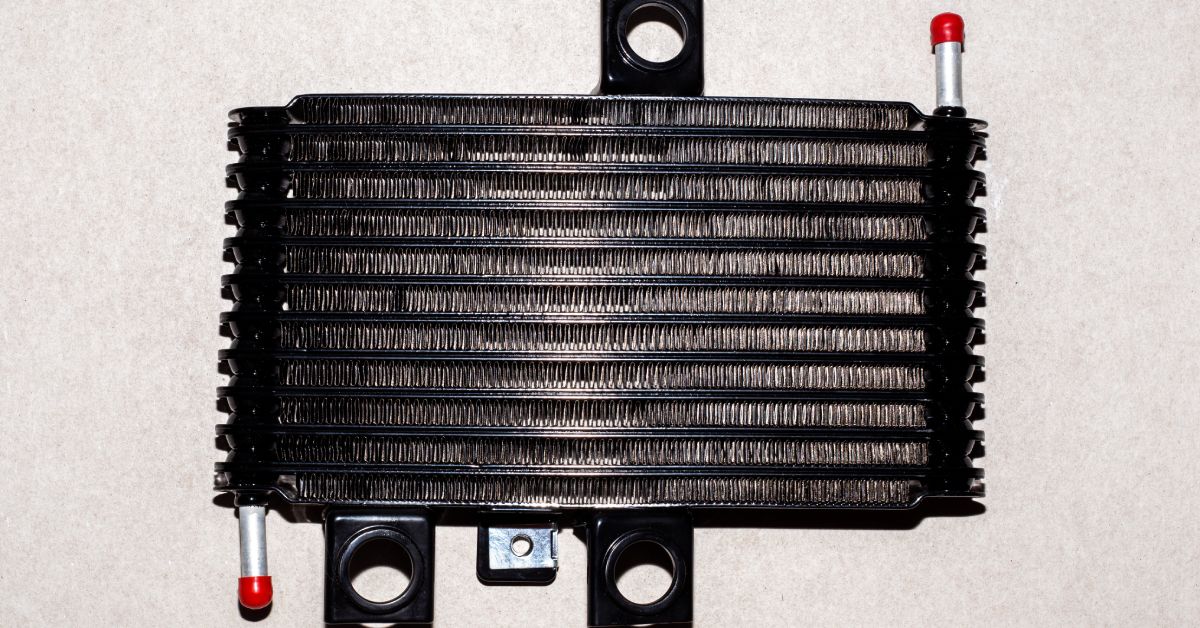 A new, black stacked-plate automatic transmission cooler is isolated against a textured, beige background.