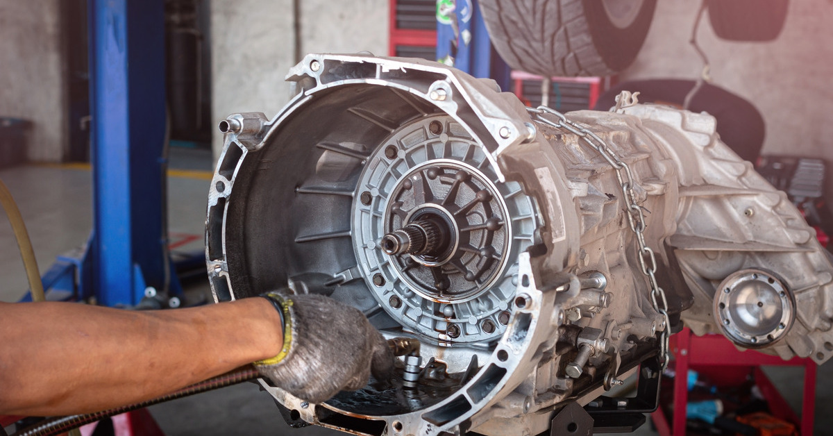 An auto mechanic's hand works on an automatic transmission. The mechanic wears a glove and holds a hose.
