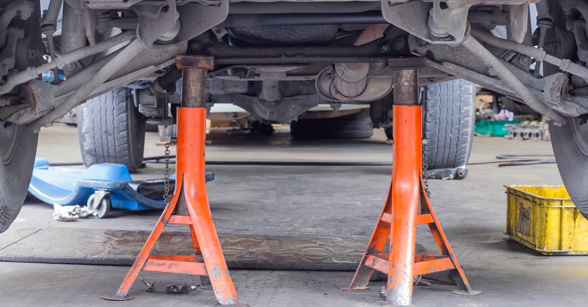 Two orange jack stands prop one end of a car up in the air. A blue mechanic's creeper sits nearby on the floor.