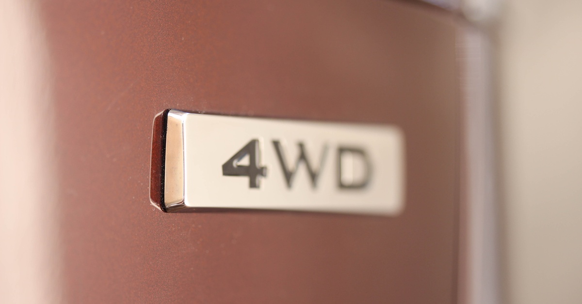 Close-up of a badge on the size of a vehicle that reads "4WD." The badge has a tan hue, while the car looks pink.