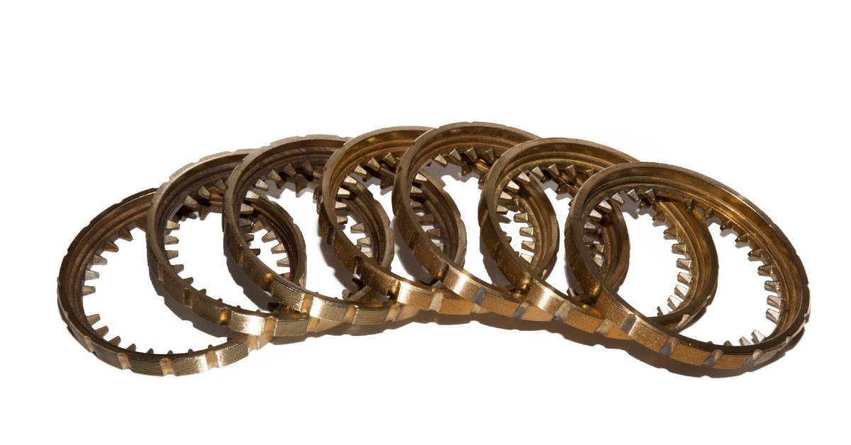 Seven car synchronizers lie together on a white background. Each of the synchronizers consists of bronze.