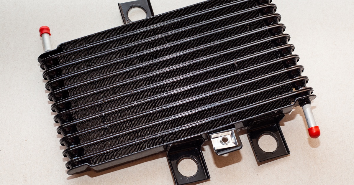 An automatic transmission cooler sits on a plain white background. It features black, white, and red components.