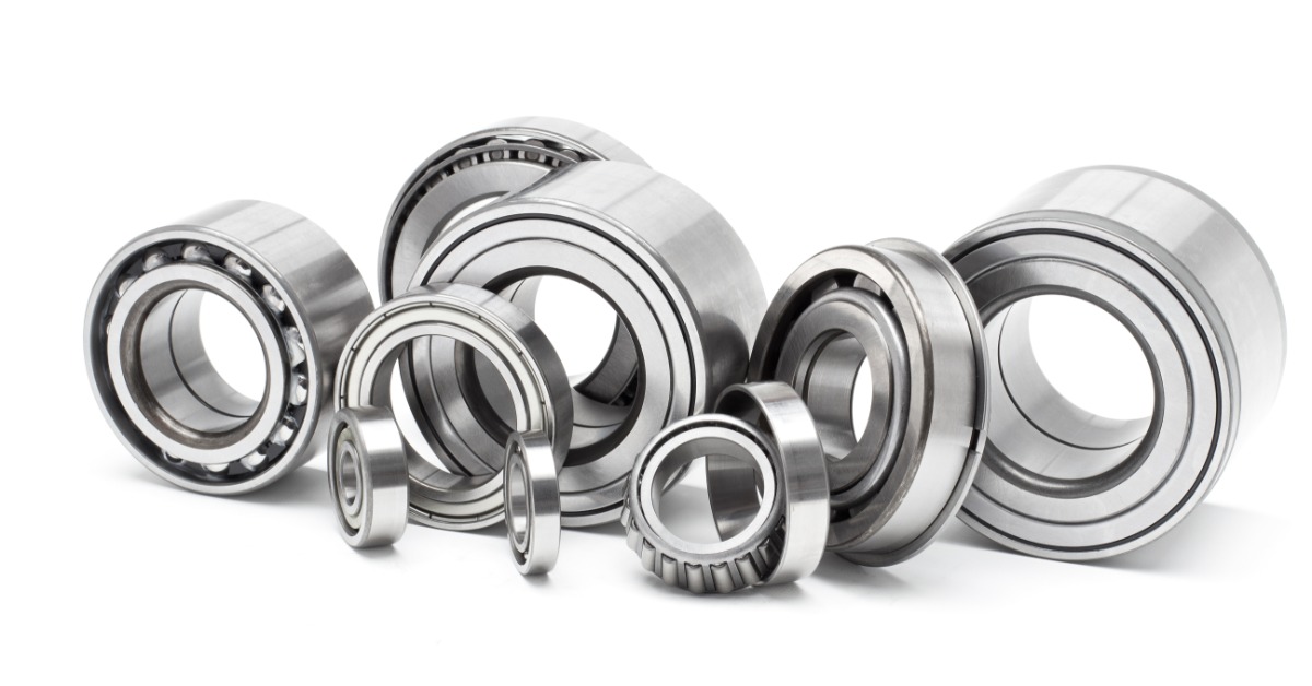 Several shiny new car bearings sit together on a white surface. Some of the bearings are taller than the others.