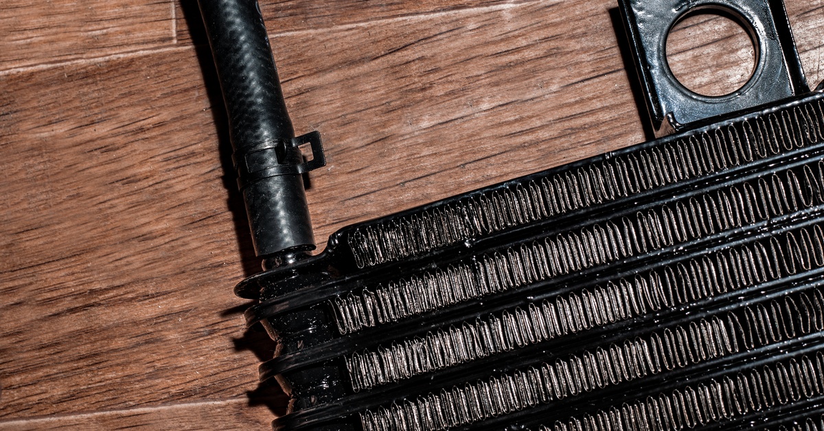 Close-up of a transmission cooler sitting on a brown wooden surface. It has a black rubber hose connected to it.