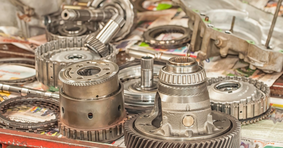 Various automatic transmission parts lie on a newspaper spread across a table, including multiple gears.