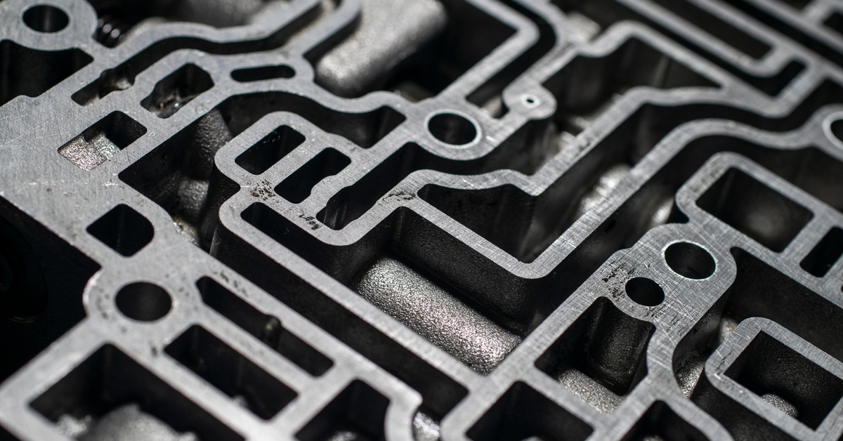 Close-up of an automatic transmission's valve body. It features numerous holes and pathways in the metal.