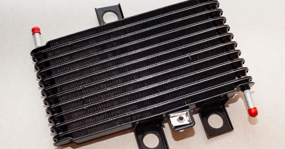 An automatic transmission cooler sits on top of a white background. It features red rubber tips on its tubes.