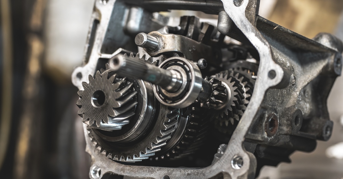Close-up of a manual transmission, sitting on a metal table with various gears visible. A silver wrench sits next to it.