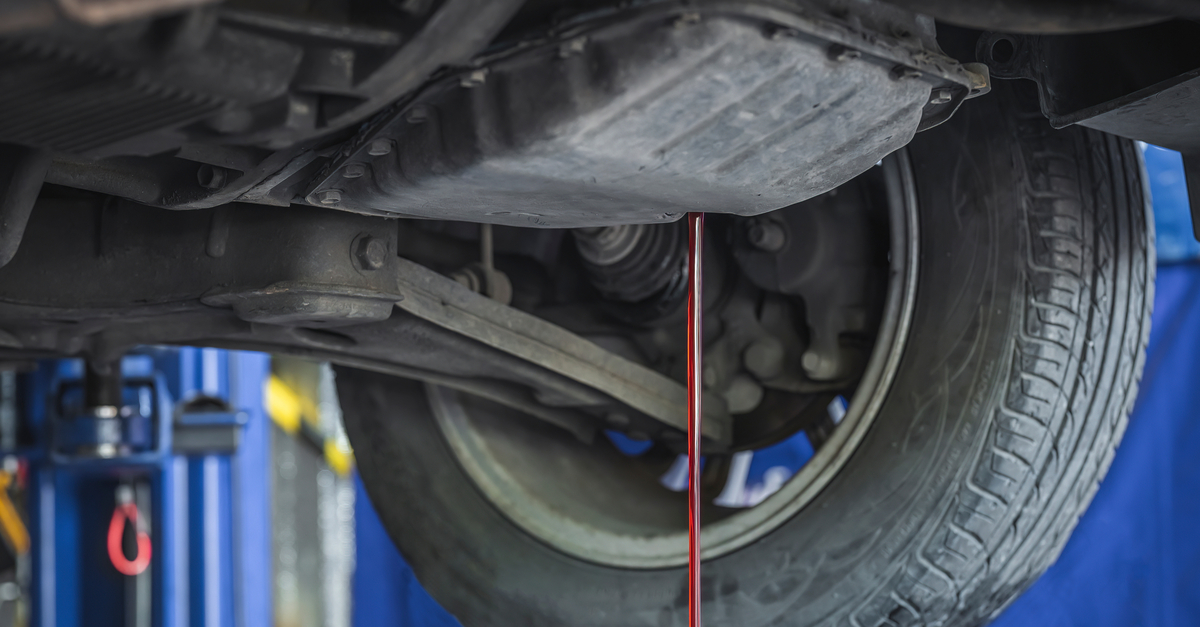 Bright red transmission fluid drains out of the bottom of a car on lifts in an auto mechanic's shop.