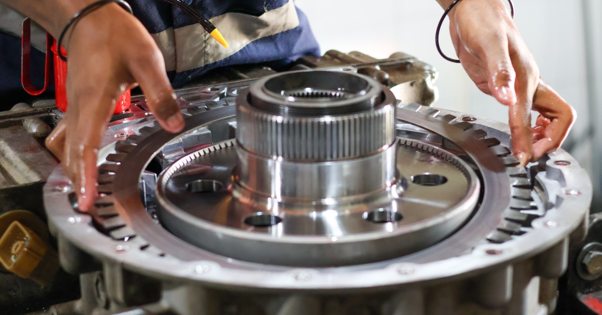 Close-up of a person's hands putting a clutch plate on a transmission assembly. All of the parts look clean.