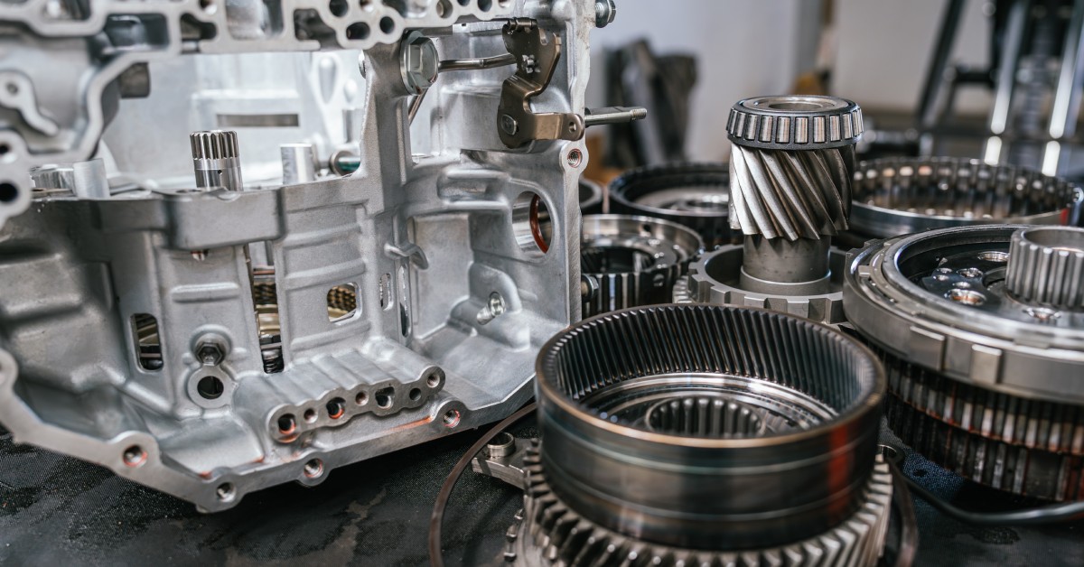 Several used transmission parts, including multiple gears, sit next to each other on a flat surface.