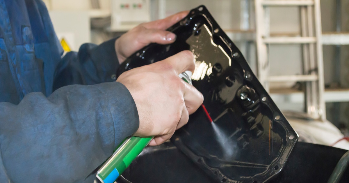 Close-up of a person's hands cleaning a car's automatic transmission pan with a spray can over a barrel.