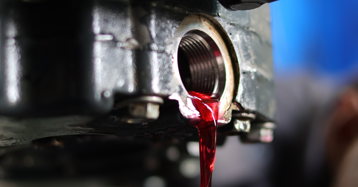 A stream of transmission fluid trickles out of an automatic transmission. The fluid looks cherry red.